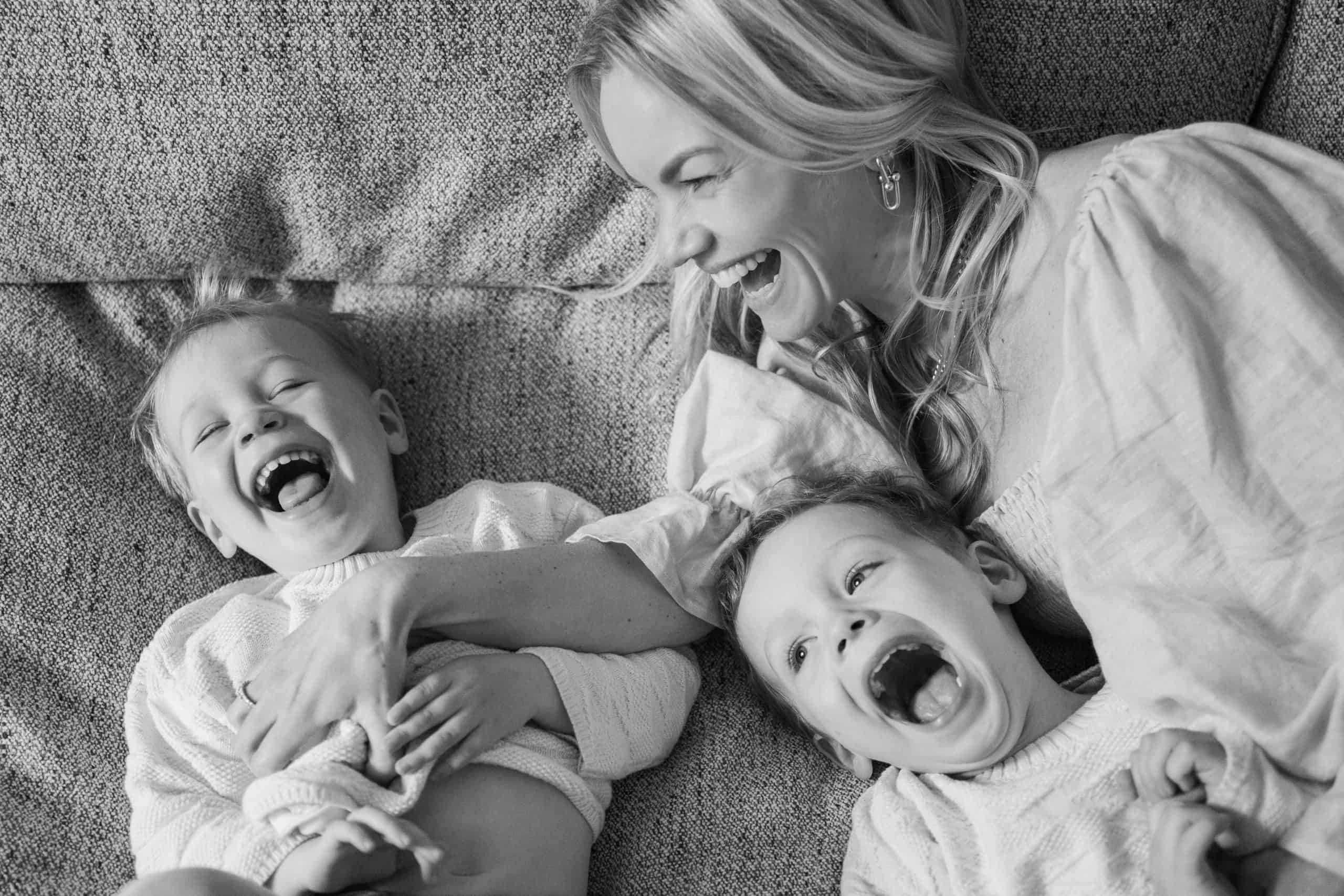 london family photography session showing black and white image of mother laughing with her sons on the sofa